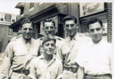 Black and white photograph of the Matz brothers in their WWII service uniforms standing at the corner of Patterson Park and Fairmont Avenue (L-R): Herbert (US Army Air Forces) , Wilbur (Army), Lester (Army), Jacob (joined the army the following year) and Charles (in front.)