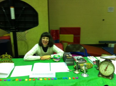 Robyn Hughes sits behind the JMM’s table at the expo.