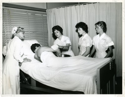 Three Sinai nursing students and their instructor stand around a patient in his hospital bed, June 1960. Accession # 2010.020.316. Courtesy of Nurses Alumnae Association of Sinai Hospital.