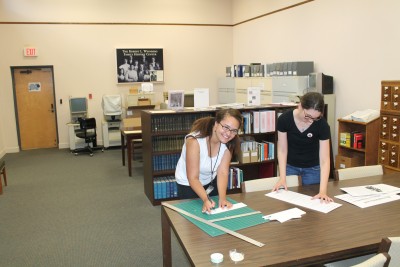 Falicia and Collections Manager Joanna in the library cutting out exhibit text.