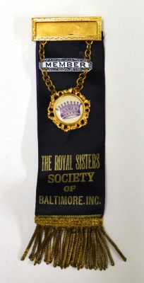 Satin badge with metal and enamel badges, and metallic fringe. “Member, The Royal Sisters Society of Baltimore, Inc.”  Gift of Helen Glaser. JMM 1998.114.9a