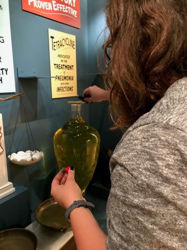 Here, Lindsay adds a few drops of food coloring to the water in one of the pharmacy show globes (yes, installing an exhibit can involve many unexpected, “other duties as assigned” tasks).