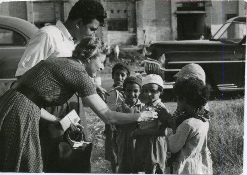 Grace Heller hands out candy to a group of Yemenite Children on an Associated mission, 1954. Her chauffeur Jack Handeh assists. JMM 1995.142.6.5