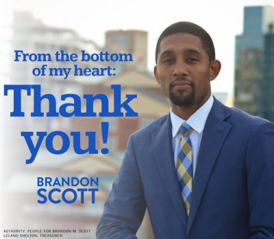 A picture of Brandon Scott, a black man wearing a suit and tie, standing outside. There are buildings out of focus in the background. The text on the image reads: "From the bottom of my heart: Thank you! Brandon Scott".