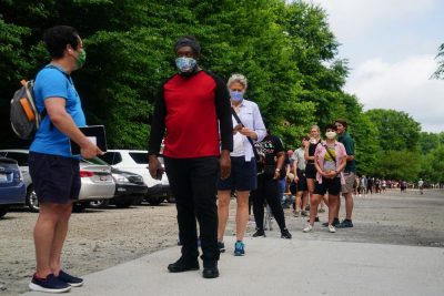 People stand in line outside, most of them wearing face masks that cover their noses and mouths. The line of people stretches far into the distance, and it's impossible to see the end.