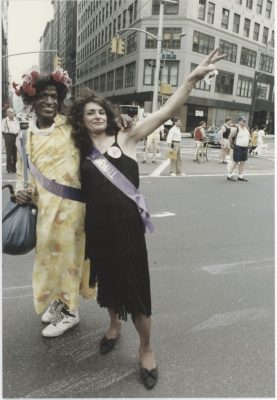 Marsha P Johnson, a black trans woman, and Sylvia Riveria, a Latina trans woman, stand together outside on a street in New York City.