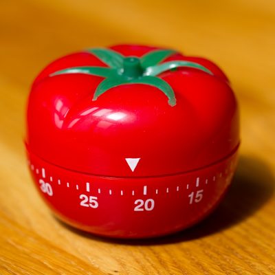 A red tomato shaped kitchen timer. It has numbers written on it to show how much time is left on the timer.