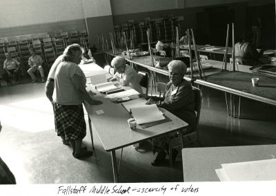 This image shows Fallstaff Middle School cafeteria where a polling site is set up. There are some people sitting at the tables to check in voters and some people signing in to vote.