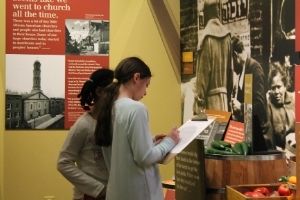 Two young students stand in the Voices of Lombard street exhibit. They look at a clipboard together that one of the students is holding.