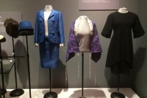 A color photograph of our Fashion Statement exhibit, focused on three garments on clothing mannequins. Included is a blue skirt suit, a purple tallit or prayer shawl, and a modest black dress.
