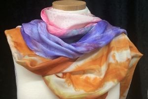 A colorful silk scarf wrapped around a clothing mannequin’s shoulders. The scarf is pink, purple, blue, and orange.