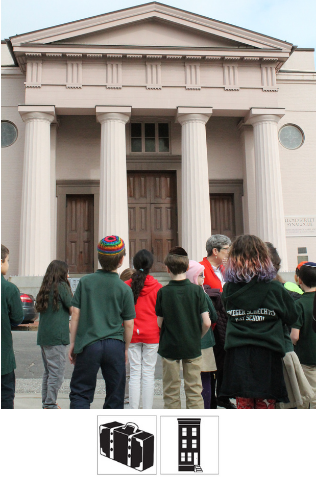 A group of students stand outside the Lloyd Street Synagogue, a large building with columns and pointed top. They look at the synagogue, listening to a tour guide.