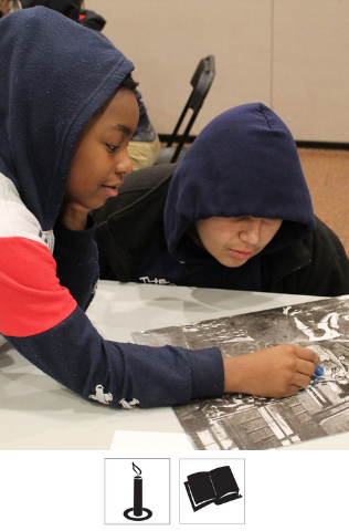 Two students sit at a table looking at a black and white image on the table. One student points to a spot in the image.