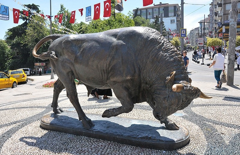Color photograph of a bronze statue of a bull with its head down and one front leg lifted.