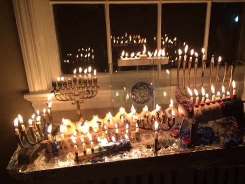 A color photograph showing 8 Hanukkah menorahs filled with mostly melted, lit candles.