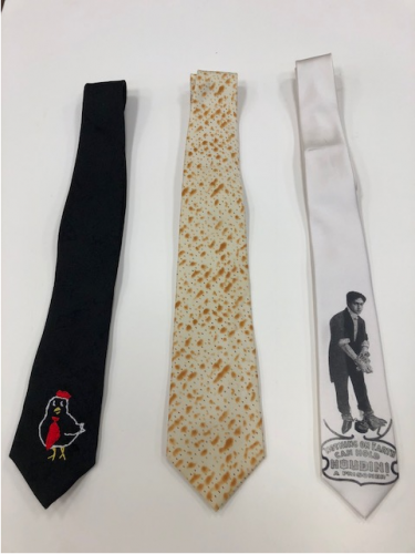 Color photo of three neckties. The first on left is a black tie with a handembroidered chicken also wearing a necktie. The middle tie is a full fabric print of matzah. The final tie on the right is white with a printage vintage photograph of Harry Houdini wearing asuit with his hands bound together.