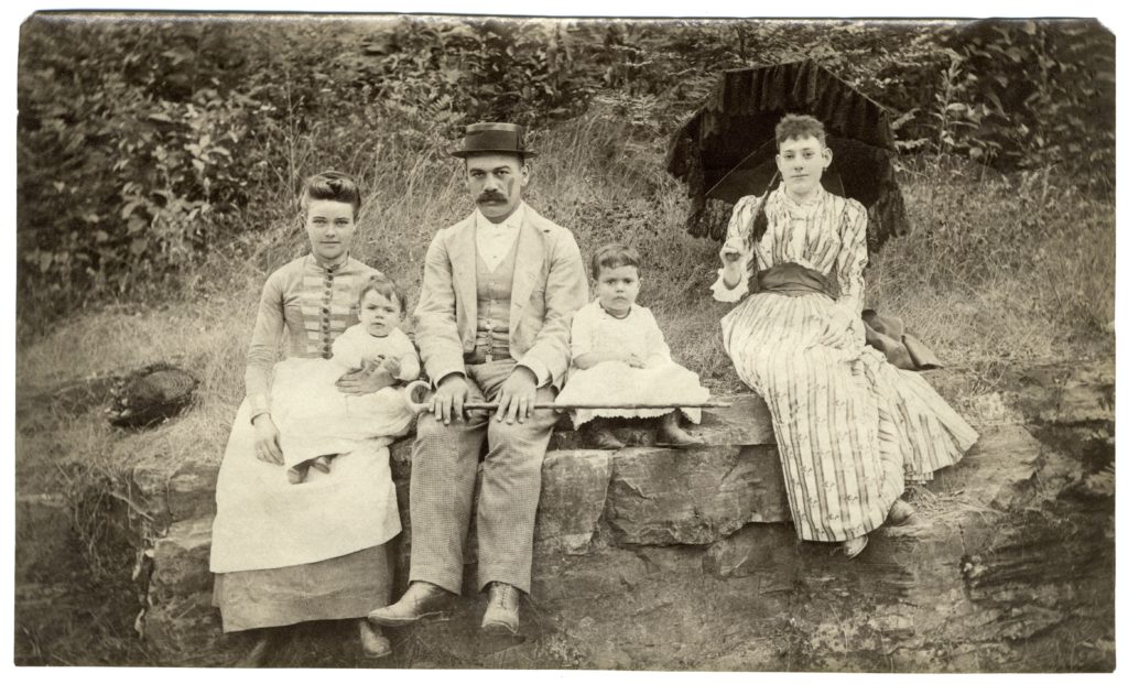 three adults and two toddlers seated on a stone wall, looking at the camera