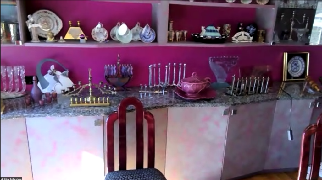 an empty chair sits in front of a set of cabinets topped with menorahs. The wall behind is painted a bright pink.