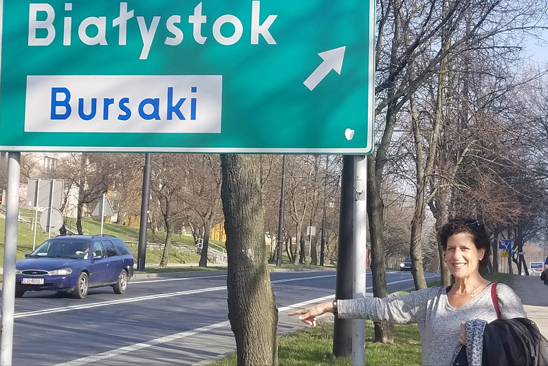 Ilene Dackman Alon pointing towards a street sign that reads “Bialystok Bursaki”