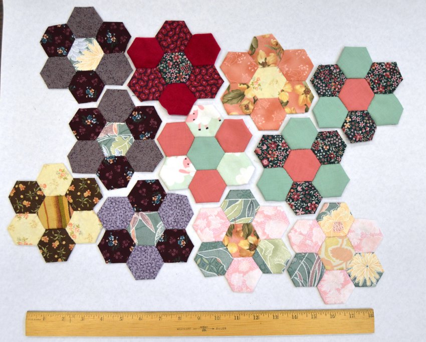 Eleven pieced flowers, each made of seven hexagons of vintage fabric, on a tabletop with a twelve-inch ruler underneath them.