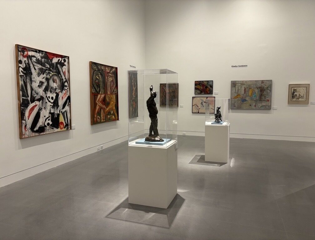 Photo of an exhibit gallery with sculptures on a pedestal and abstract art hanging on walls in the background