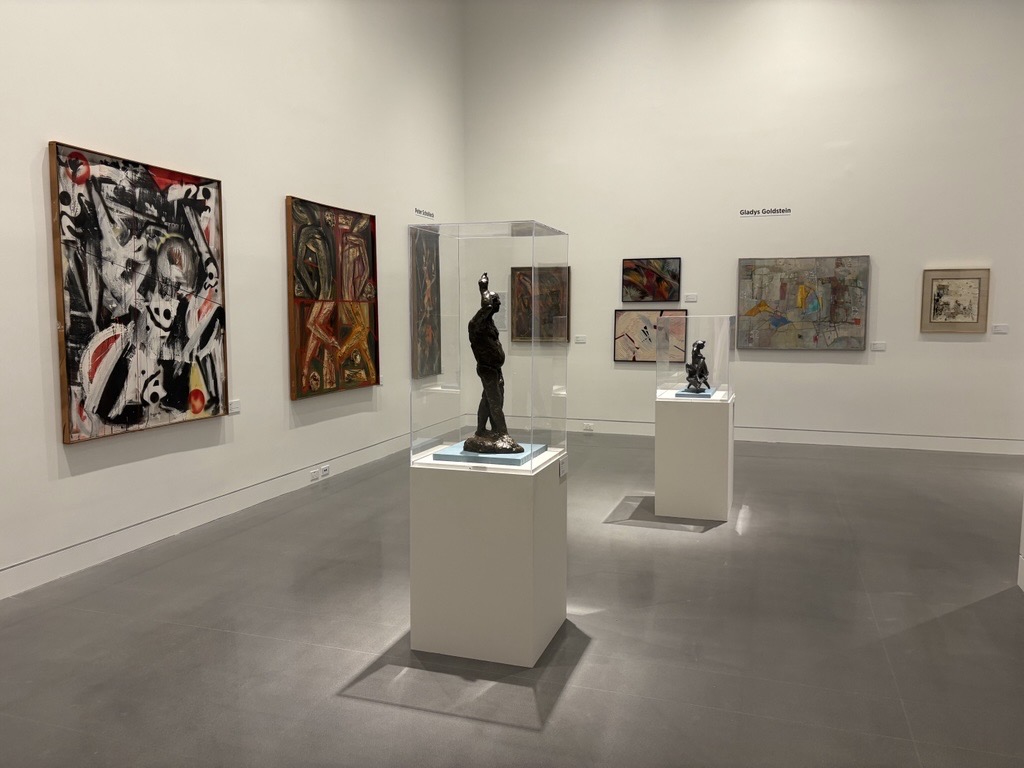 Photo of an exhibit gallery with sculptures on a pedestal and abstract art hanging on walls in the background
